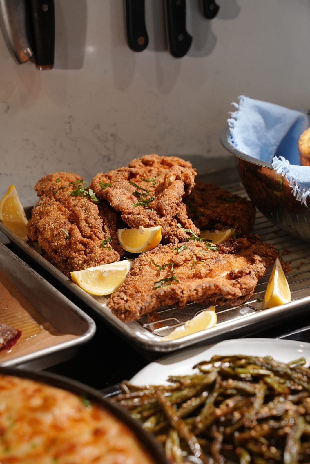 Breaded fried cutlets on a wire cooling rack garnished with lemon wedges and herbs. - Hungry Mockingbird