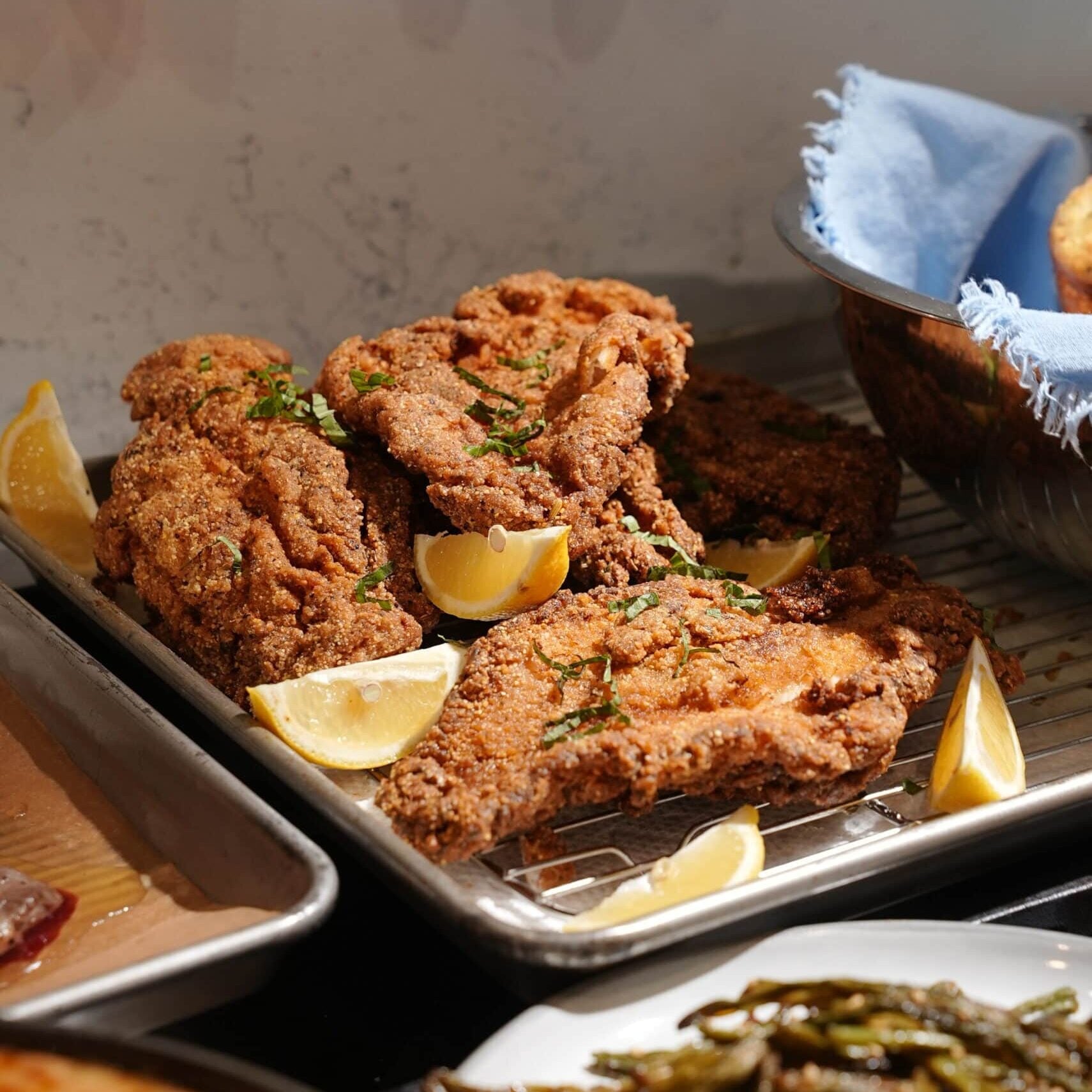 Breaded fried cutlets on a wire cooling rack garnished with lemon wedges and herbs. - Hungry Mockingbird
